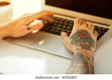 Young Man With Tattoo Using Laptop At The Table At Home