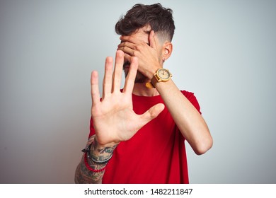 Young Man With Tattoo Wearing Red T-shirt Standing Over Isolated White Background Covering Eyes With Hands And Doing Stop Gesture With Sad And Fear Expression. Embarrassed And Negative Concept.