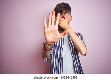 Young Man With Tattoo Wearing Striped Shirt Standing Over Isolated Pink Background Covering Eyes With Hands And Doing Stop Gesture With Sad And Fear Expression. Embarrassed And Negative Concept.