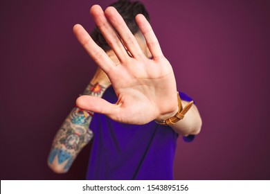 Young Man With Tattoo Wearing T-shirt Standing Over Isolated Purple Background Covering Eyes With Hands And Doing Stop Gesture With Sad And Fear Expression. Embarrassed And Negative Concept.