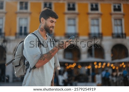 Young man with tattoos and backpack using mobile phone in commerce square, lisbon, portugal