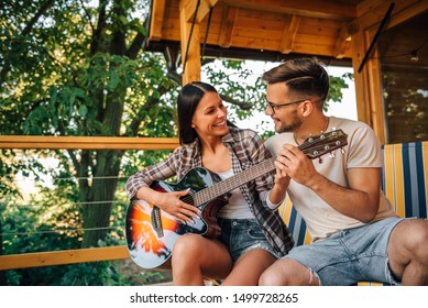 Young man teaching girl how to play guitar on a vacation at wooden cabin terrace. - Powered by Shutterstock