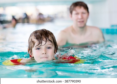 Young Man Teaching His Little Active Son To Swim In An Indoor Swimming Pool. Active Happy Kid Boy Wearing Safe Swimmies. Family Time.