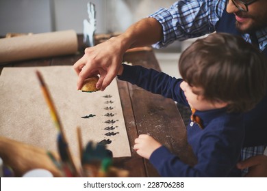 Young man teaching his son how to print on paper with help of potato and gouache - Powered by Shutterstock