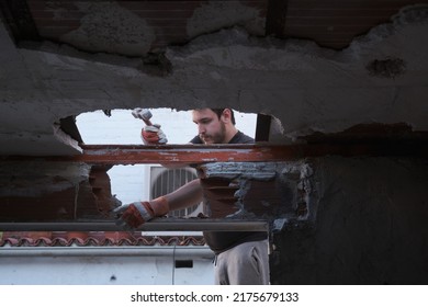 Young Man Tearing The Ceiling Of A House Down Using A Mallet.