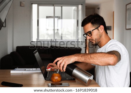 young man telecommuting from home. using computer and having a hot drink