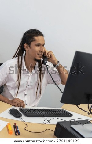 Young man telephonist with dreadlocks working at his desk communicating by phone