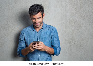 Young man texting message on smart phone isolated on grey background. Smiling latin man holding smartphone and looking at it. Happy hispanic man writing a message on the  phone. - Powered by Shutterstock