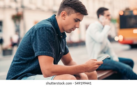 Young Man Texting On A Bench In The City