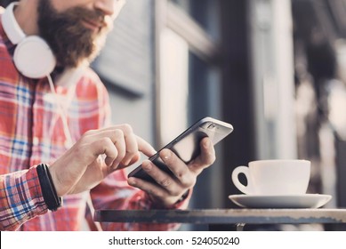 Young man texting on his smartphone in the city. Close up of cheerful adult using mobile phone in a cafe