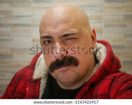 A young man with a thick mustache winking 