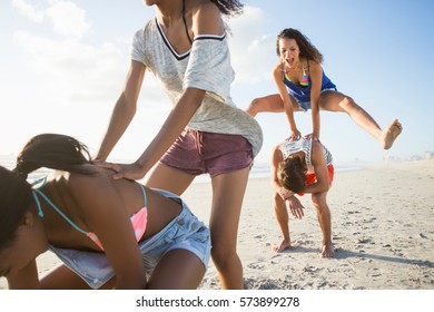 Young Man And Three Female Friends Playing Leapfrog On Beach, Cape Town, South Africa