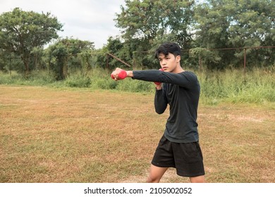 A young man throws a quick left jab. Weighted shadow boxing with a pair of dumbbells at an outdoor field.