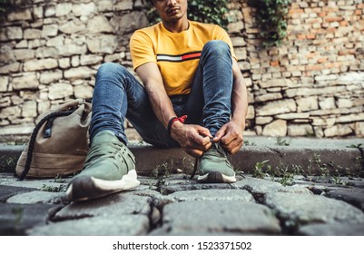 Young Man A Young Man Tied Laces In Sneakers ,sitting On Concrete Stairs. Hipster Guy Tie Down Shoe Lace.Comfortable Footwear For City Walk