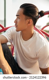 Young Man With Top Knot Sitting In The Park Under The Sunset