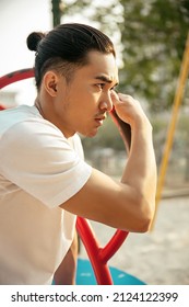 Young Man With Top Knot Sitting In The Park Under The Sunset