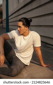 Young Man With Top Knot Sitting In The City Under The Sunset