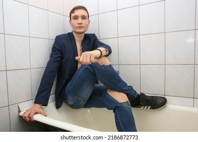 A Young Man In Torn Jeans Is Sitting In The Bathtub