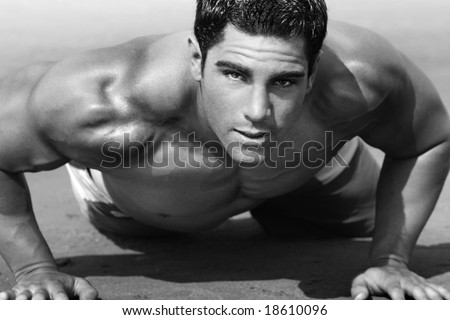 young man with torso doing push-ups on the beach