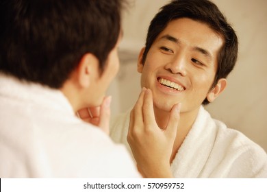 Young Man Touching His Face, Looking In Mirror
