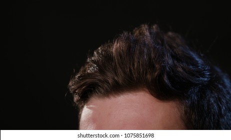 A young man touching his hair against a black background. Close-up macro shot