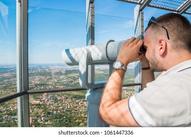 Young man tourist looking through telescope on top of Avala observation tower deck, Belgrade, Serbia. Enjoying beautiful mountain landscape. Travel and buildings concept. - Shutterstock ID 1061447336