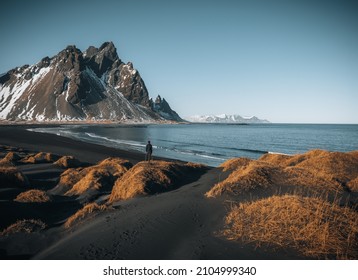 Young man tourist standing at beach during sunset runrise and gorgeous reflection of Vestrahorn mountain on Stokksnes cape in Iceland. Beautiful snow covered mountains. Location: Stokksnes cape