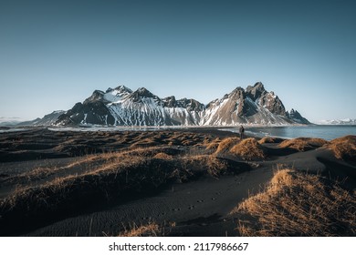 Young man tourist standing at beach during sunset runrise and gorgeous reflection of Vestrahorn mountain on Stokksnes cape in Iceland. Beautiful snow covered mountains. Location: Stokksnes cape
