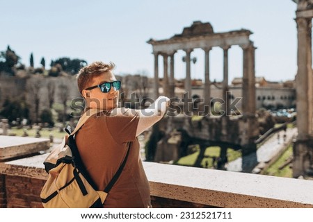 Young man tourist in sunglasses resting at Roman Forum. Historical imperial Foro Romano from panoramic point of view, Italy. Concept of travel, tourism and vacation in city.