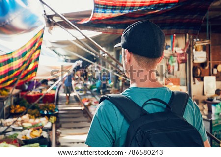 Young man (tourist) walking to open market along the railroad track. Maeklong railway market close to Bangkok in Thailand.