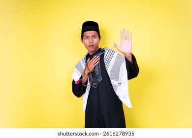 A young man in traditional Muslim attire gestures with one hand raised, while the other rests on his chest, against a vibrant yellow backdrop.  His expression conveys sincerity and openness. - Powered by Shutterstock - Get 15% off with code: PIKWIZARD15