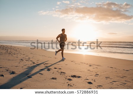 Young man training on the beach in morning. Young man on morning run outdoors.