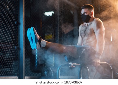 Young man trains  with push-up bars. Guy wearing a  face mask during his workout in gym. Self-isolation during COVID. Healthy Lifestyle and Sport Concepts. - Shutterstock ID 1870708609