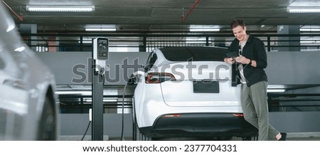 Young man travel with EV electric car to shopping center parking lot charging in downtown city showing urban sustainability lifestyle by green clean rechargeable energy of electric vehicle innards Foto stock © 