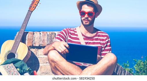 Young man travel portrait using notebook on hill top ocean background - Globe trotter hipster guy with sun glasses and pc relaxing on summer day outdoors - Concept of freedom with blue vintage filter