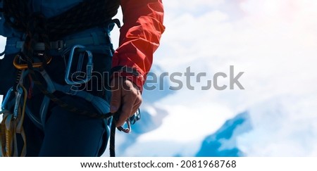 Young man traveler alpinist climbs to the top of a snowy mountain with climbing equipment, harness, carbines, rope.
