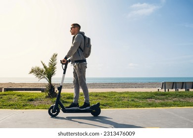 Young man traveler riding e-scooter along the sea coast and beach at sunny summer day. Male driving electric scooter outdoors. Sustainable lifestyle concept - Powered by Shutterstock