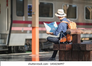 A Young Man Traveler Sitting With Map Choose Where To Travel And Bag Waiting For Train, 