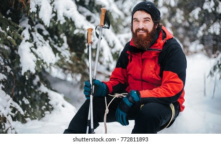 Young Man Traveler  In Snowy Forest. Happy Sport Man With Beard Take A Rest In Mountains. Adventure, Travel, Tourism, Hike And People Concept. Extreme Winter Sports. Winter.