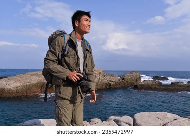 A young man travelling on stony area. Landscape  photographer  with the camera in his hands walking on rocky terrain and wearing backpack