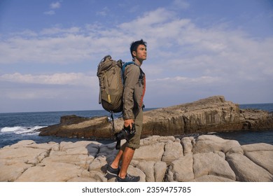 A young man travelling on stony area. Landscape  photographer  with the camera in his hands walking on rocky terrain and wearing backpack