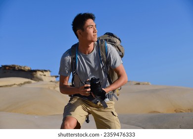 A young man travelling on stony area. Landscape  photographer  with the camera in his hands walking on rocky terrain and wearing backpack