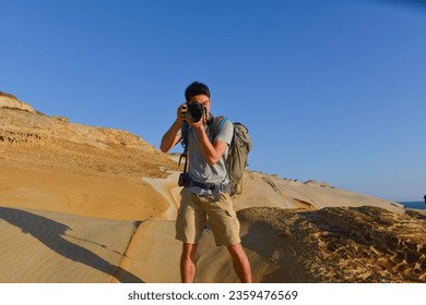A young man travelling on stony area. Landscape  photographer  with the camera in his hands walking on rocky terrain and wearing backpack