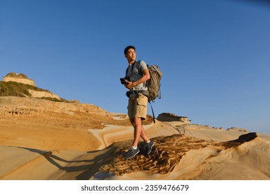 A young man travelling on stony area. Landscape  photographer  with the camera in his hands walking on rocky terrain and wearing backpack - Powered by Shutterstock