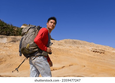 A young man travelling on stony area. Landscape  photographer  with the camera in his hands walking on rocky terrain and wearing backpack