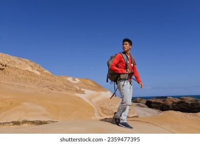 A young man travelling on stony area. Landscape  photographer  with the camera in his hands walking on rocky terrain and wearing backpack