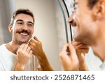 Young man trims his mustache with scissors in the bathroom in front of the mirror.