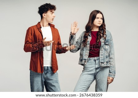 Young man trying to explain something with open hands to an annoyed woman gesturing to stop talking on a light gray background