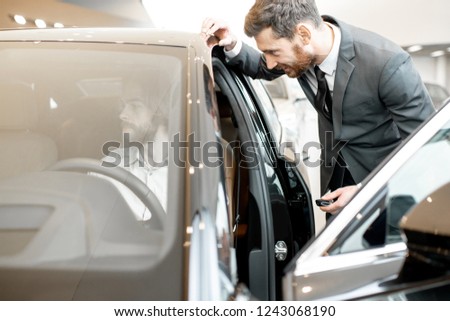 Young man trying a new car sitting on the driver seat talking with salesperson in the showroom