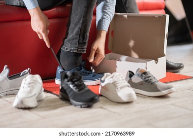 Young Man Trying On Sport Shoes In Shop, Sitting In The Fitting Room Of A Modern Sporting Goods Store